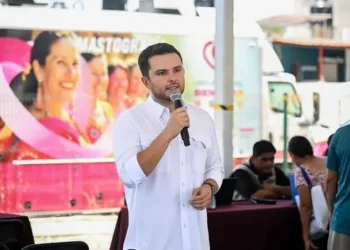 Hombre con camisa blanca habla con micrófono frente a una unidad móvil de mastografía