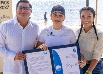 Tres personas muestran en la playa el certificado Blue Flag de la Playa 88 de Playa del Carmen