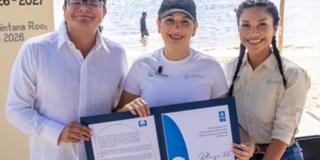 Tres personas muestran en la playa el certificado Blue Flag de la Playa 88 de Playa del Carmen