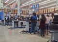 Cajeras atienden de pie a clientes en las cajas de una tienda de autoservicio.