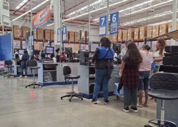 Cajeras atienden de pie a clientes en las cajas de una tienda de autoservicio.