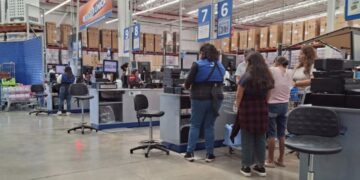 Cajeras atienden de pie a clientes en las cajas de una tienda de autoservicio.