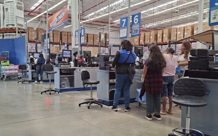 Cajeras atienden de pie a clientes en las cajas de una tienda de autoservicio.