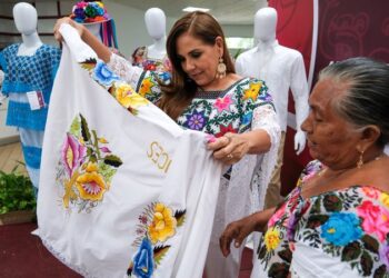 Mara Lezama observa una prenda bordada junto a una artesana durante la premiación en Chetumal