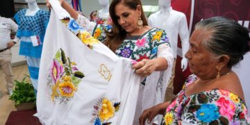 Mara Lezama observa una prenda bordada junto a una artesana durante la premiación en Chetumal