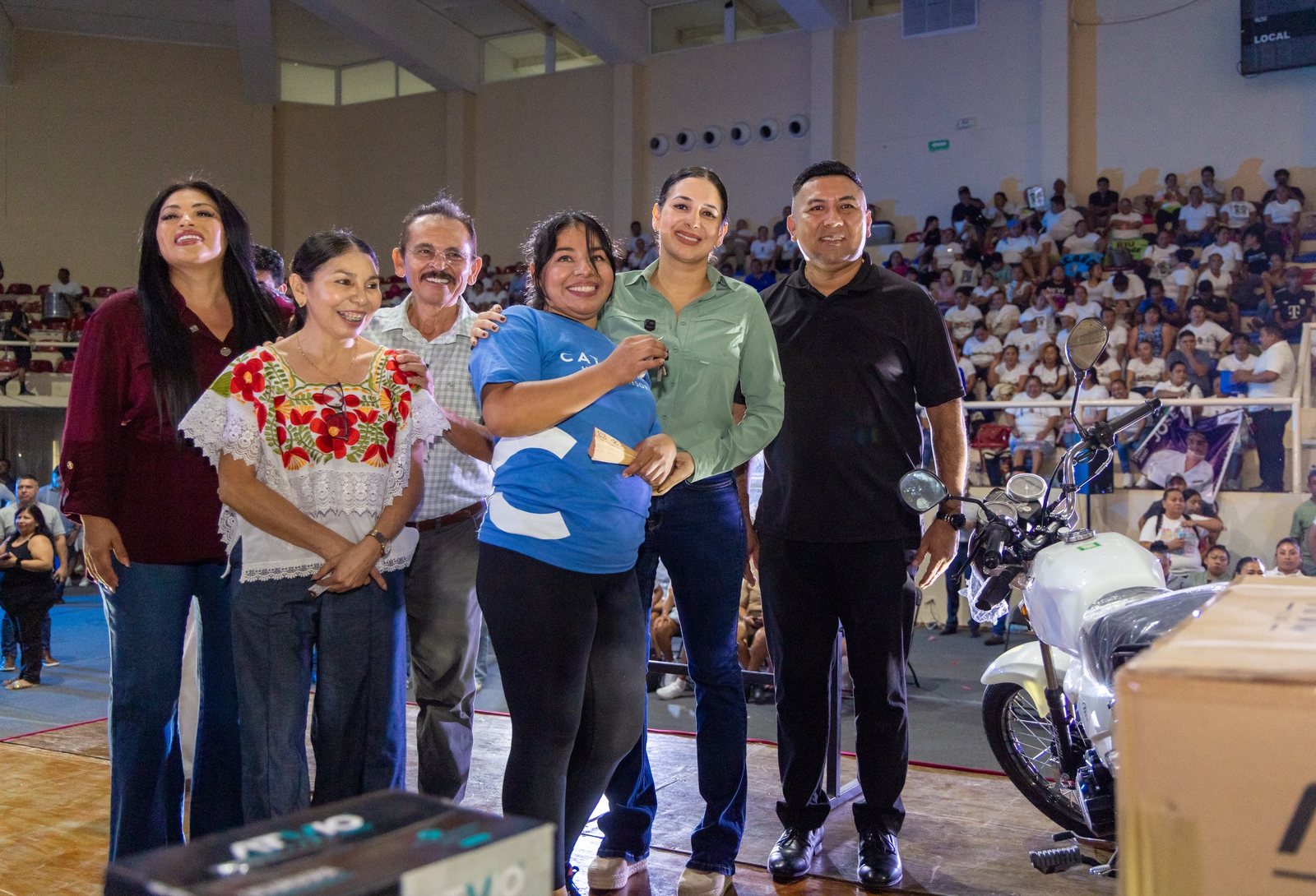 Trabajadora hotelera con la presidenta municipal Estefanía Mercado junto a una motocicleta en el Concurso Tendido de Camas