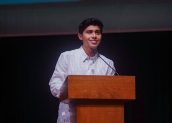Joven con guayabera blanca habla desde un atril de madera en la ceremonia de graduación de la UQROO Campus Playa del Carmen